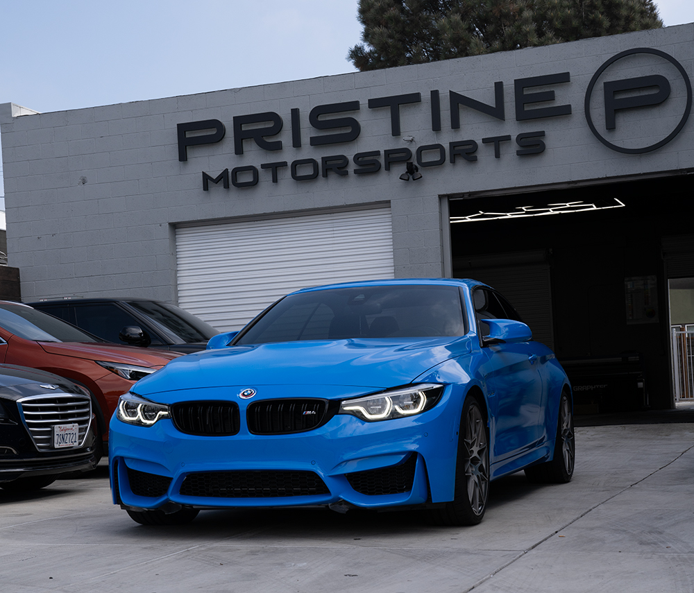 A blue BMW in front of Pristine motorsports